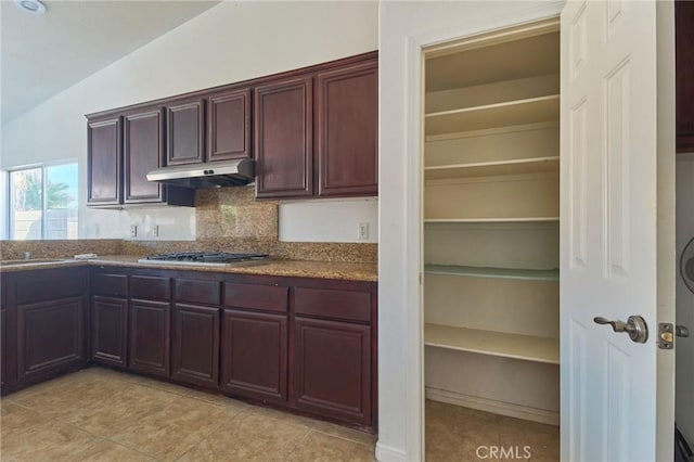 kitchen with stainless steel gas cooktop, tasteful backsplash, lofted ceiling, light tile patterned flooring, and under cabinet range hood