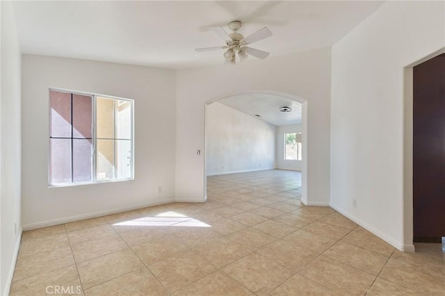 spare room with arched walkways, ceiling fan, light tile patterned floors, and baseboards