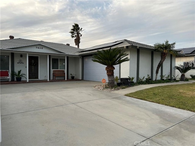 view of front facade featuring a garage, driveway, roof mounted solar panels, a front lawn, and stucco siding