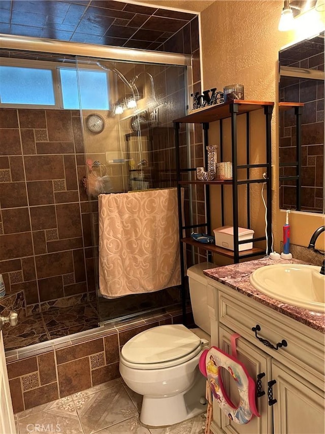 bathroom featuring a textured wall, a tile shower, vanity, and toilet