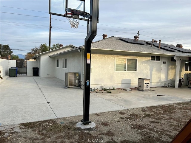 rear view of house with stucco siding, a shingled roof, solar panels, central air condition unit, and a gate