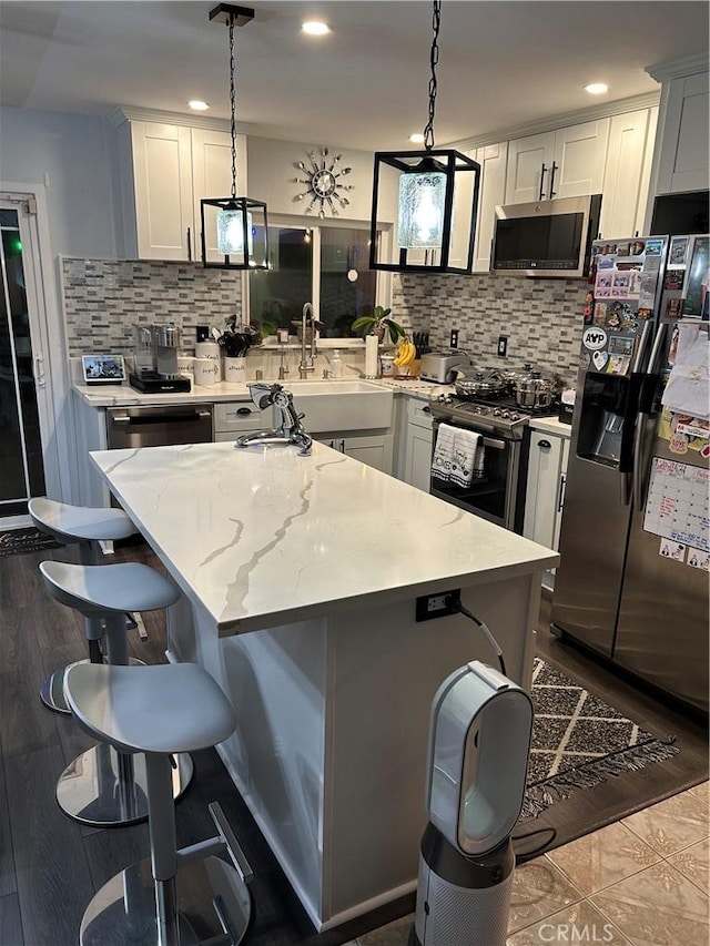 kitchen featuring a kitchen island, appliances with stainless steel finishes, white cabinets, and decorative light fixtures