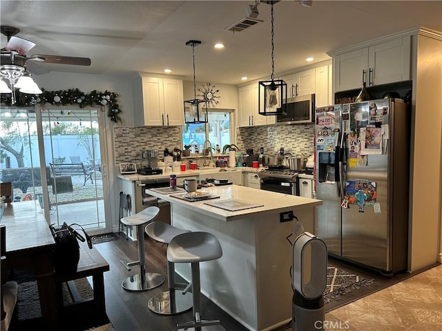 kitchen with white cabinets, appliances with stainless steel finishes, a center island, light countertops, and pendant lighting