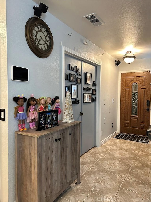 entrance foyer featuring a textured ceiling, a textured wall, and visible vents