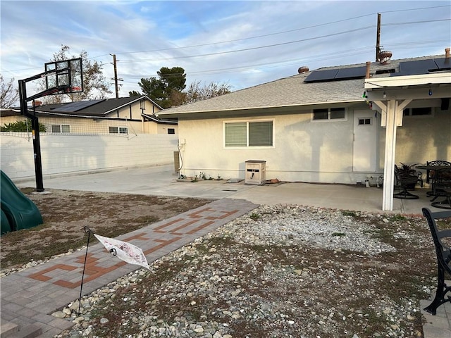 rear view of property featuring solar panels, roof with shingles, a patio area, and stucco siding