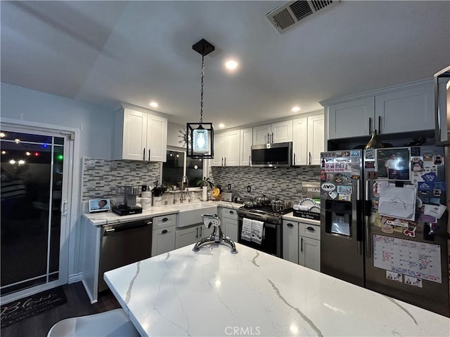 kitchen featuring light stone counters, pendant lighting, stainless steel appliances, visible vents, and white cabinetry