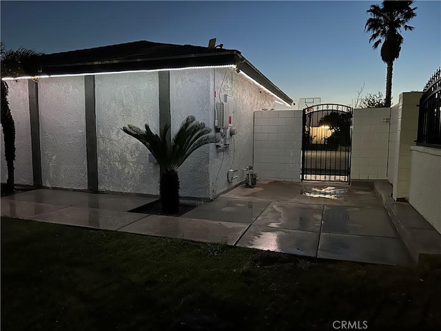 property exterior at dusk featuring fence, a gate, and stucco siding