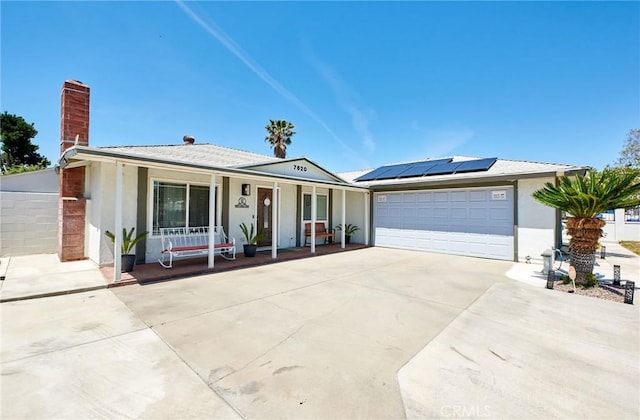 ranch-style home featuring driveway, a porch, an attached garage, roof mounted solar panels, and stucco siding