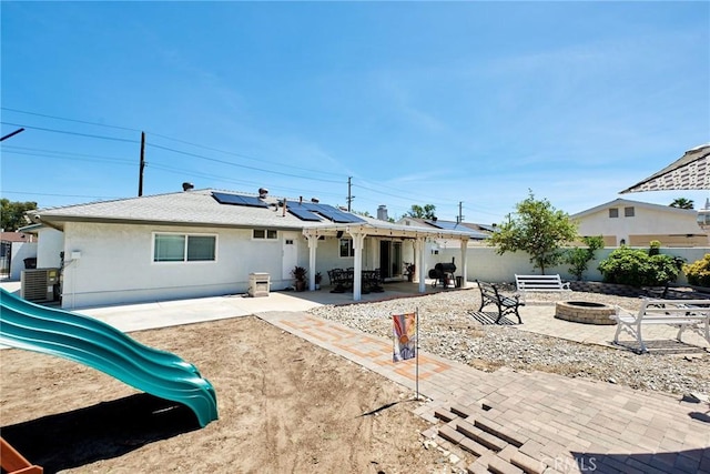 back of house featuring a patio area, a playground, an outdoor fire pit, stucco siding, and solar panels