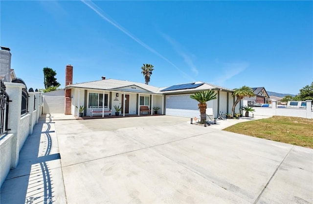 view of front of property featuring roof mounted solar panels, an attached garage, concrete driveway, and fence