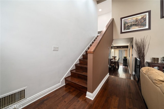 stairway featuring a towering ceiling, baseboards, visible vents, and wood finished floors