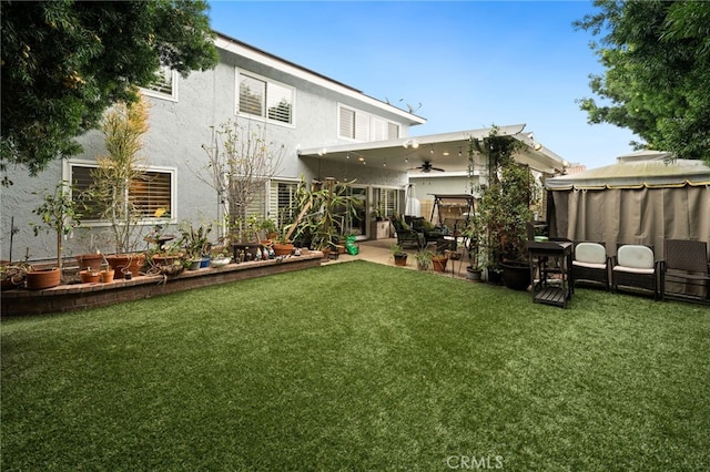 back of house featuring ceiling fan, a patio, a yard, and stucco siding