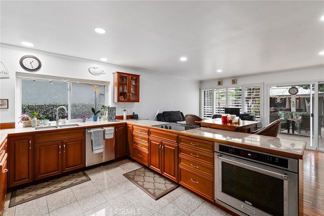 kitchen featuring brown cabinetry, appliances with stainless steel finishes, a peninsula, a sink, and recessed lighting