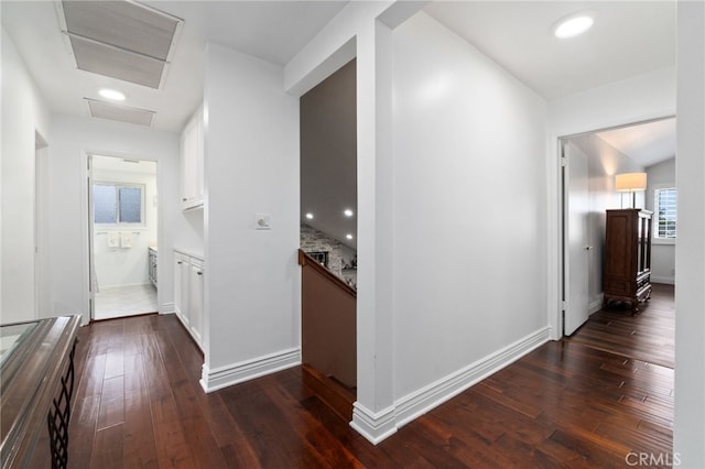 hallway featuring attic access, baseboards, and dark wood-style flooring