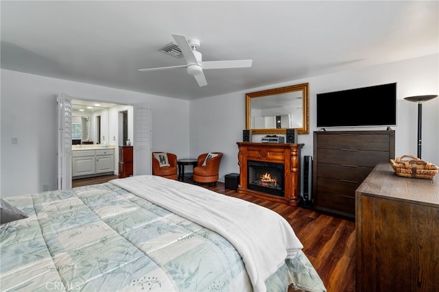 bedroom featuring visible vents, dark wood finished floors, a ceiling fan, a lit fireplace, and ensuite bath