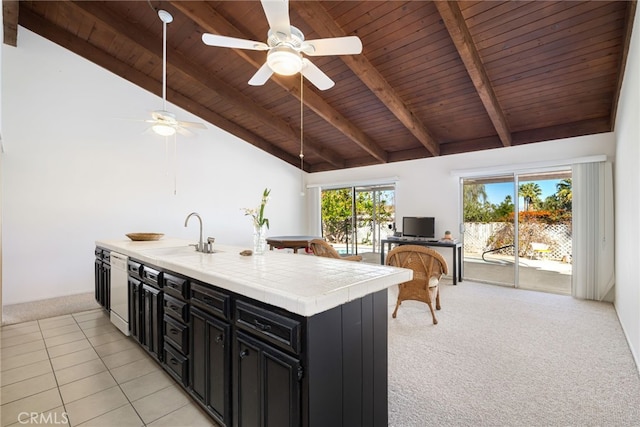 kitchen with light colored carpet, dark cabinets, a sink, tile counters, and beamed ceiling