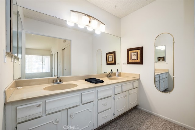 bathroom with double vanity, a textured ceiling, baseboards, and a sink