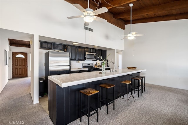 kitchen with stainless steel appliances, wood ceiling, light carpet, dark cabinetry, and a kitchen breakfast bar