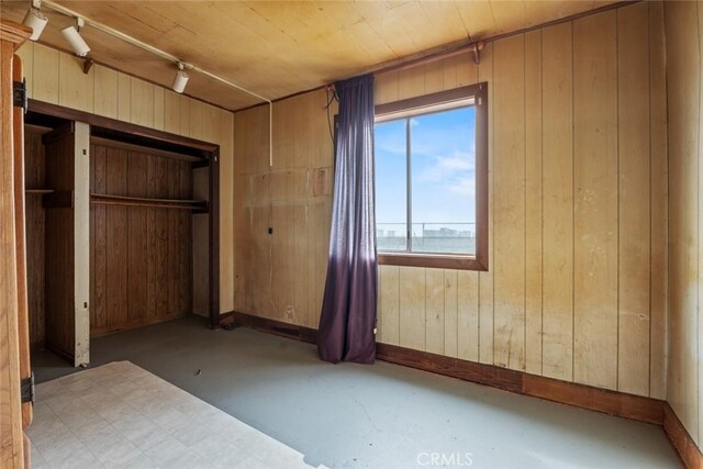 unfurnished bedroom featuring track lighting, wood walls, baseboards, and concrete flooring