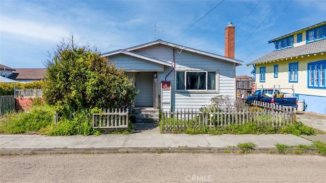 bungalow-style home featuring a chimney and a fenced front yard