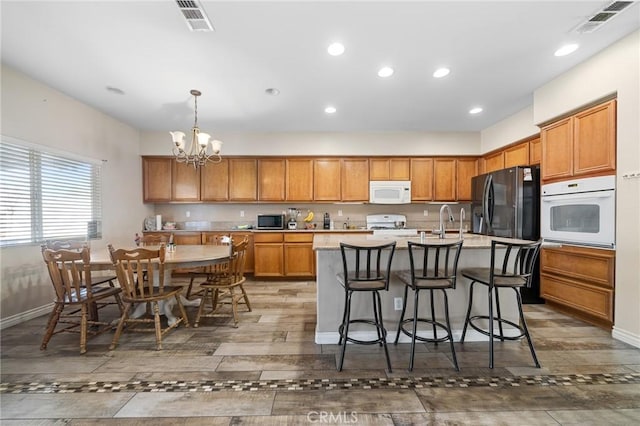 kitchen featuring white appliances, a center island with sink, visible vents, decorative light fixtures, and light countertops