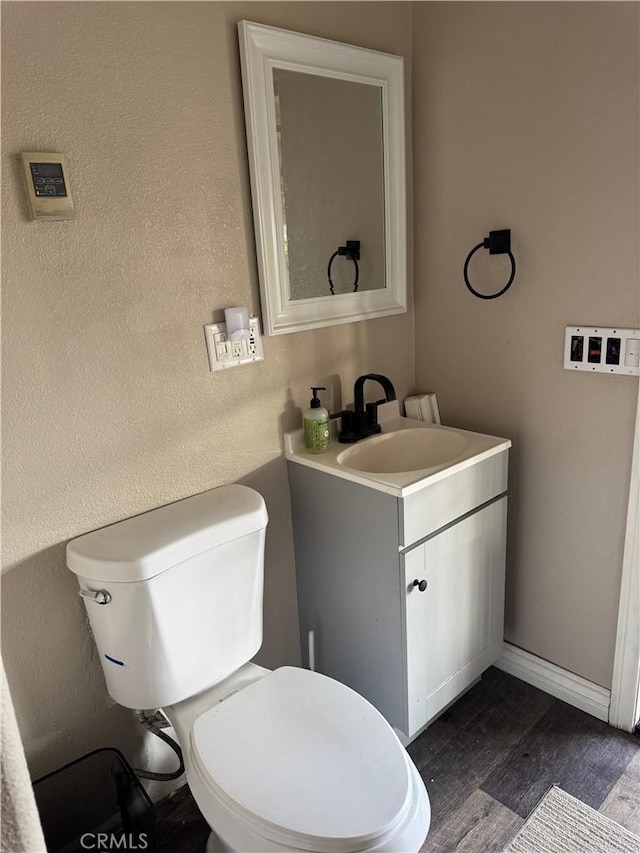 half bathroom with toilet, baseboards, wood finished floors, and vanity