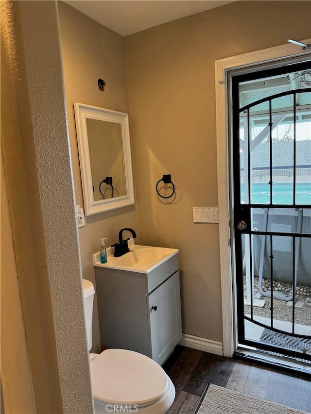 half bath with baseboards, vanity, toilet, and wood finished floors