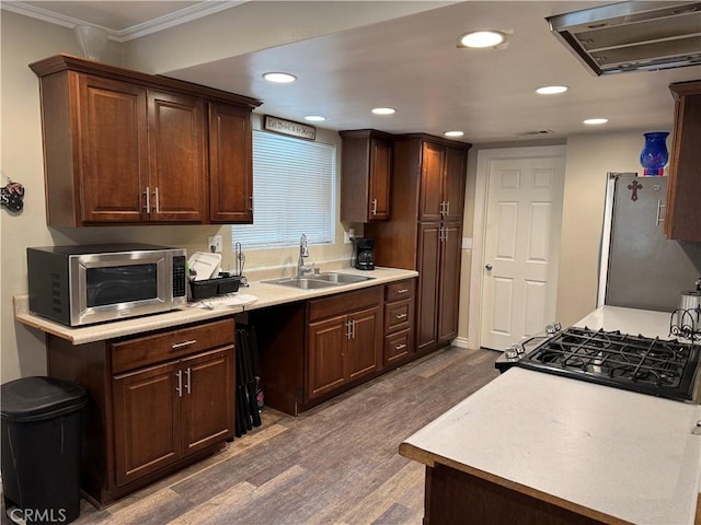 kitchen featuring stainless steel appliances, light countertops, dark wood-type flooring, a sink, and wall chimney exhaust hood