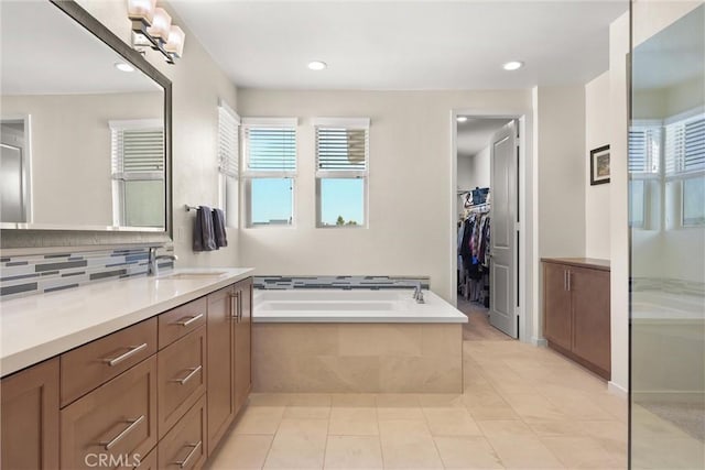 bathroom with a spacious closet, decorative backsplash, vanity, a bath, and tile patterned floors