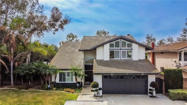 view of front of home featuring an attached garage, a tile roof, concrete driveway, stucco siding, and a front yard