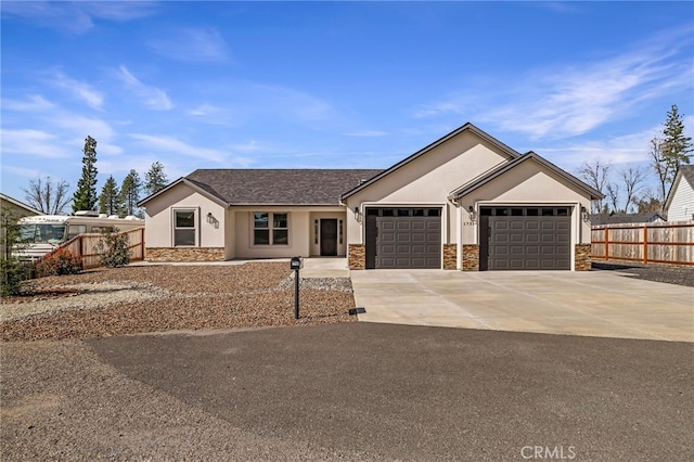 view of front of house featuring an attached garage, fence, driveway, stone siding, and stucco siding