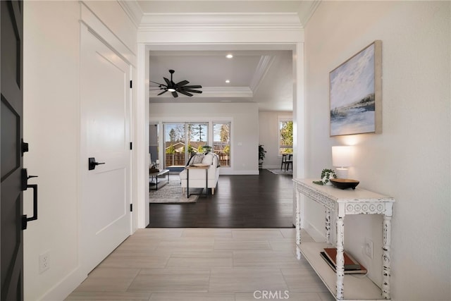 corridor with recessed lighting, a raised ceiling, ornamental molding, wood finished floors, and baseboards