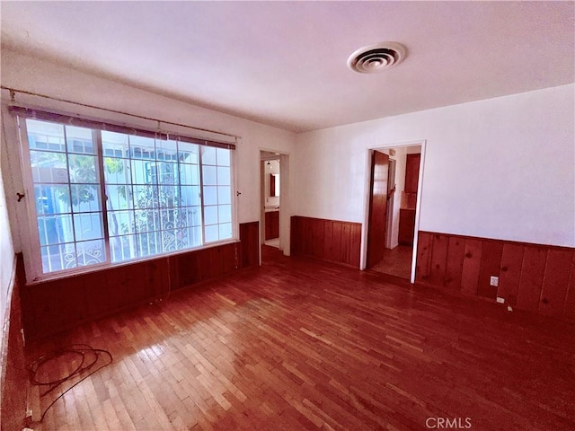 spare room featuring a wainscoted wall, visible vents, wooden walls, and wood finished floors