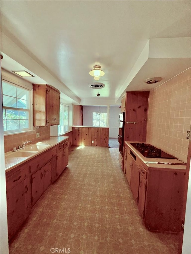 kitchen featuring black stovetop, decorative backsplash, visible vents, and a healthy amount of sunlight