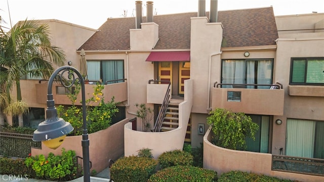 view of front facade with a shingled roof, a sink, and stucco siding