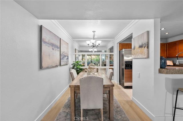 dining space featuring wood finished floors, crown molding, baseboards, and an inviting chandelier