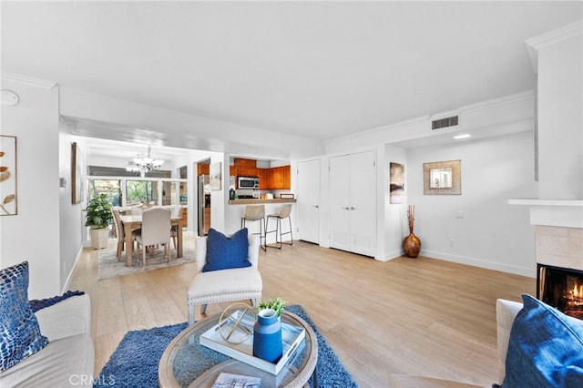 living room with ornamental molding, light wood-type flooring, a chandelier, and a fireplace