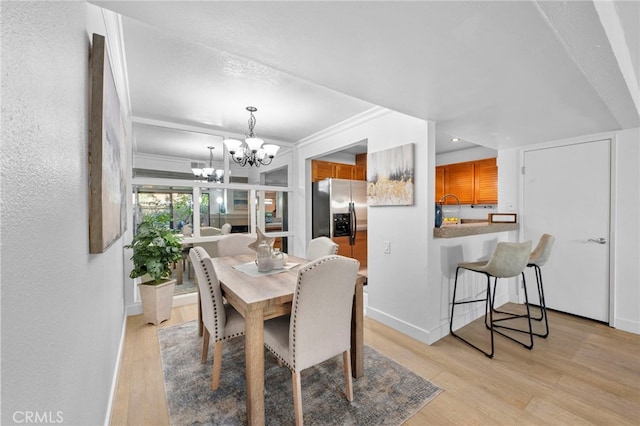 dining area with an inviting chandelier, light wood-style flooring, baseboards, and crown molding