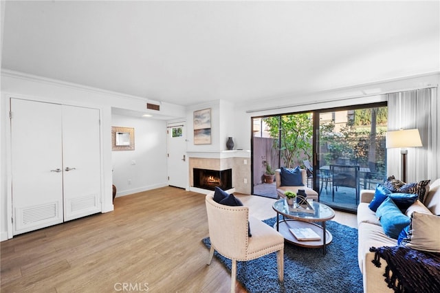 living room featuring a warm lit fireplace, visible vents, baseboards, ornamental molding, and light wood-type flooring