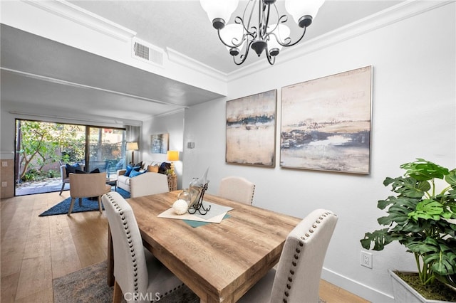 dining space with ornamental molding, visible vents, a notable chandelier, and wood finished floors