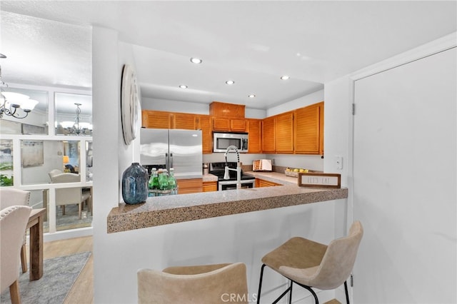 kitchen featuring stainless steel appliances, a peninsula, light countertops, and a notable chandelier