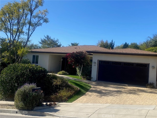 ranch-style home featuring decorative driveway, an attached garage, and stucco siding