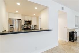 kitchen with a peninsula, dark countertops, white cabinetry, and appliances with stainless steel finishes