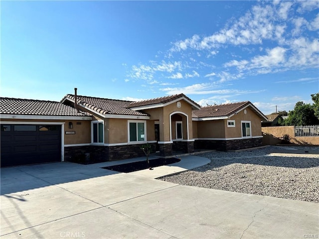 view of front of property with an attached garage, fence, stone siding, driveway, and stucco siding