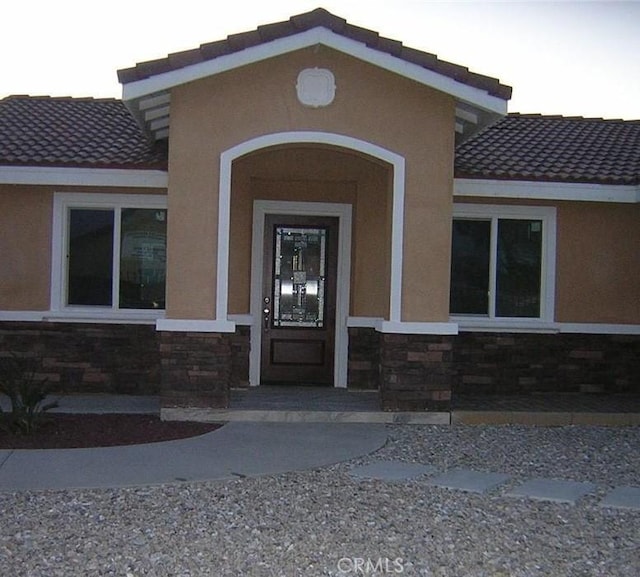 property entrance with stone siding, a tile roof, and stucco siding