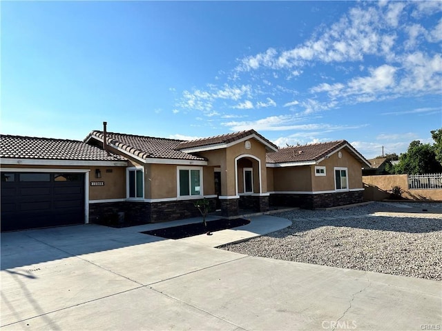 view of front of property with stucco siding, an attached garage, fence, stone siding, and driveway