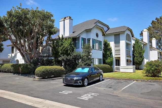 view of front of house with uncovered parking, a chimney, a front yard, and stucco siding