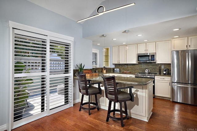 kitchen featuring a peninsula, appliances with stainless steel finishes, backsplash, and dark wood-type flooring