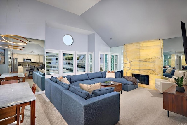 living room with light carpet, high vaulted ceiling, a fireplace, and an inviting chandelier