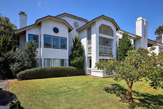 view of front of home featuring a front lawn, a chimney, and stucco siding